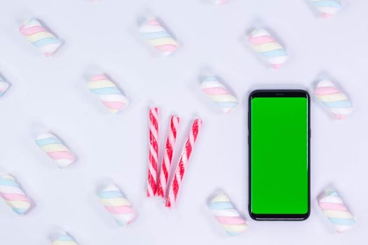 Phone mobile telephone with a vertical green screen. White background with twisted marshmallow pattern. Chroma key smartphone technology.