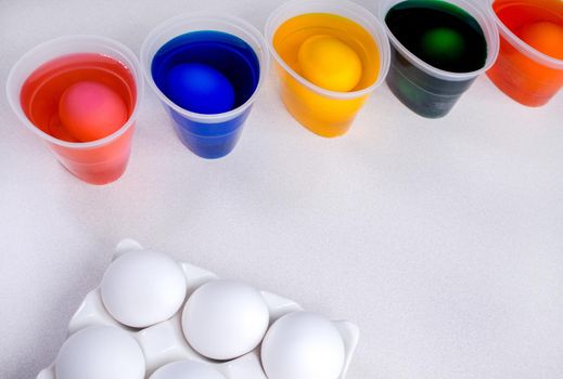 Tools for painting eggs for easter, eggs box, cups of colorful paint, easter eggs, plate, brushes and paints on the table side view.