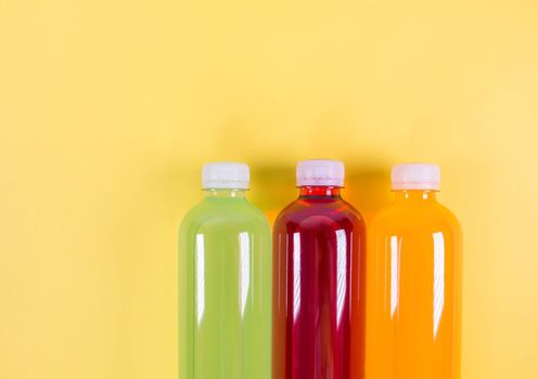 Bottles of orange, green, red smoothie on yellow background. Top view. Detox summer drink. Healthy fresh juice bottle. Vegan and vegetarian concept.