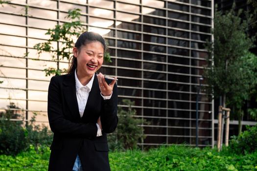 asiatic business woman laughing talking by phone in a park next to an office building, concept of technology and communication, copy space for text