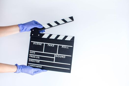 Woman in blue disposable rubber gloves holding movie clapper. Influence of pandemic on cinematography