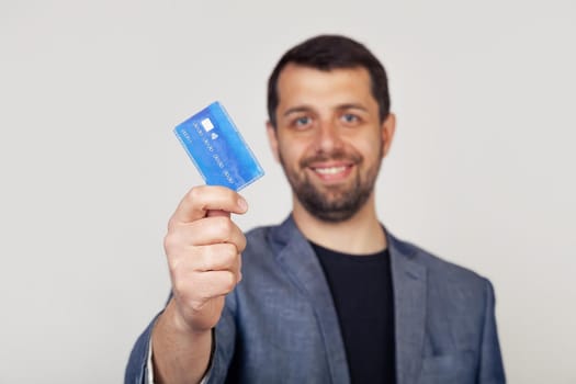 Young businessman man with beard smiling, holding credit card with happy face, standing and smiling with confident smile, showing teeth.