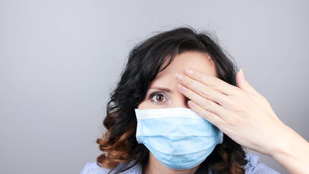 Woman wearing protection face mask against coronavirus covering one eye with hand. Woman in a mask hiding her eyes. Medical mask, Close up shot, Select focus, Prevention from covid19