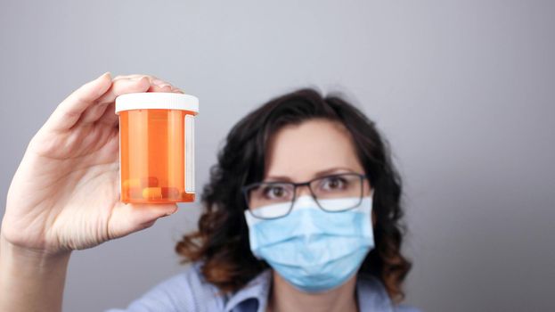 Woman wearing protection face mask against coronavirus and glasses. Woman in a mask showing medicine pill, vaccine, antibiotic. Medical mask, Close up shot, Select focus, Prevention from covid19