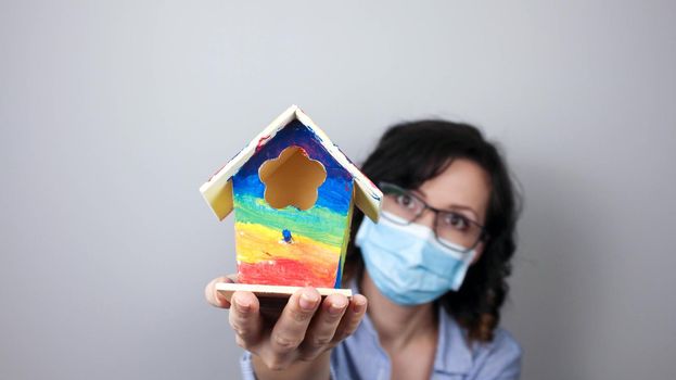Woman wearing protection face mask against coronavirus and glasses. Woman in a mask showing rainbow house. We will be okay. Medical mask, Close up shot, Select focus, Prevention from covid19
