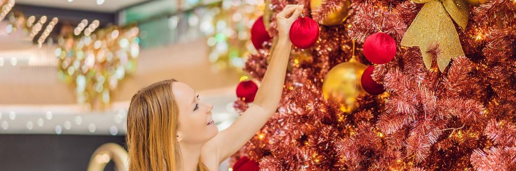 Woman hangs a decoration on the red Christmas tree. Red Christmas tree on the background of lights. BANNER, LONG FORMAT