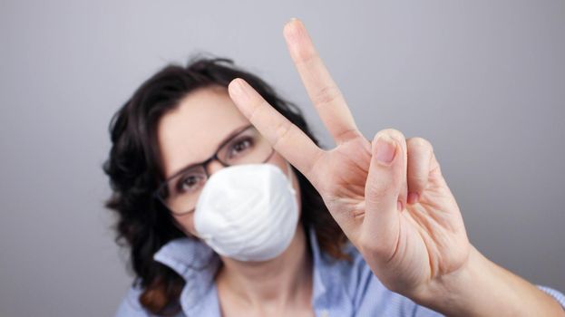 Young caucasian woman wearing face mask standing against gray wall showing and pointing up with fingers number two while smiling confident and happy. Peace sign.