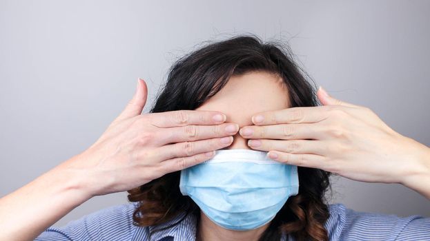 Woman wearing protection face mask against coronavirus covering her eyes with hands. Woman in a mask hiding her eyes. Medical mask, Close up shot, Select focus,