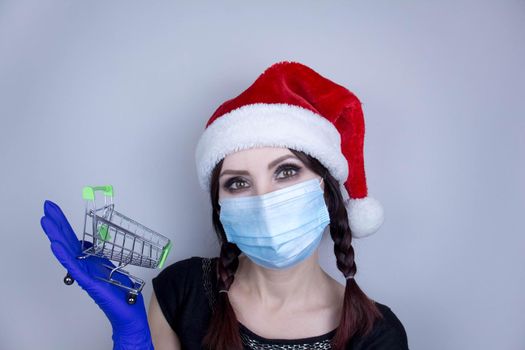 Woman wearing protection face mask against coronavirus. Woman in a mask and Christmas hat and holding shopping cart.