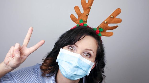 Woman wearing protection face mask against coronavirus. Woman in a mask and deer horns headband. Funny Christmas accessory. Medical mask, Close up shot, Select focus, Prevention from covid19