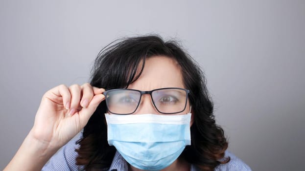 Woman wearing protection face mask against coronavirus and misted glasses. Woman in a mask looking in a mirror. Medical mask, Close up shot, Select focus, Prevention from covid19