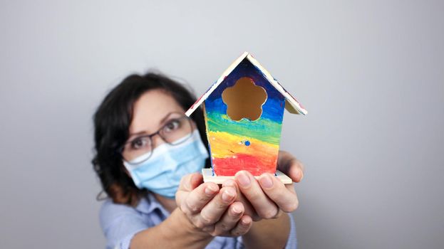 Woman wearing protection face mask against coronavirus and glasses. Woman in a mask showing rainbow house. We will be okay. Medical mask, Close up shot, Select focus, Prevention from covid19