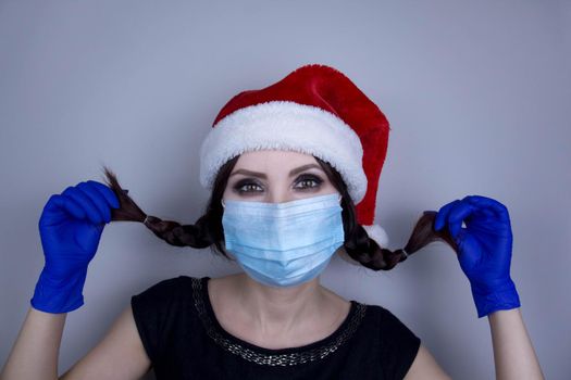 Woman wearing protection face mask against coronavirus. Woman in a mask and Christmas hat. Funny Christmas accessory. Medical mask, Medical gloves, Close up shot, Select focus, Prevention from covid19