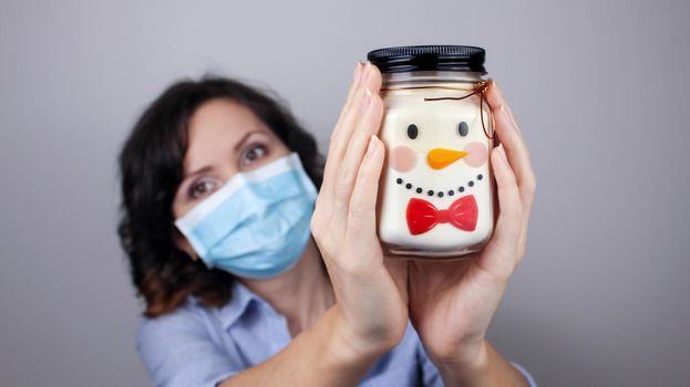 Woman wearing protection face mask against coronavirus. Woman in a mask showing snowman. Can with a Christmas face. We will be okay. Medical mask, Close up shot, Select focus, Prevention from covid19