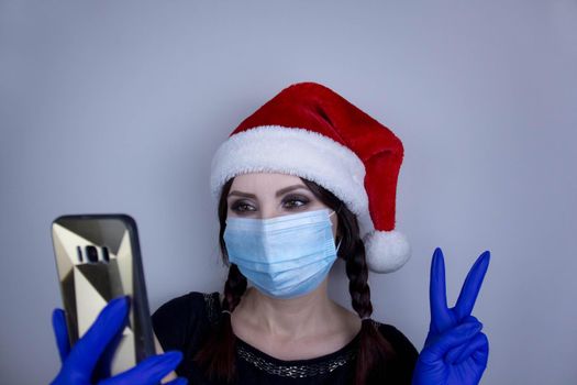 Woman wearing protection face mask against coronavirus. Woman in a mask and Christmas hat taking selfie. Funny Christmas accessory. Medical mask, Close up shot, Select focus, Prevention from covid19