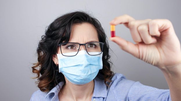 Woman wearing protection face mask against coronavirus and glasses. Woman in a mask showing medicine pill, vaccine. Medical mask, Close up shot, Select focus, Prevention from covid19