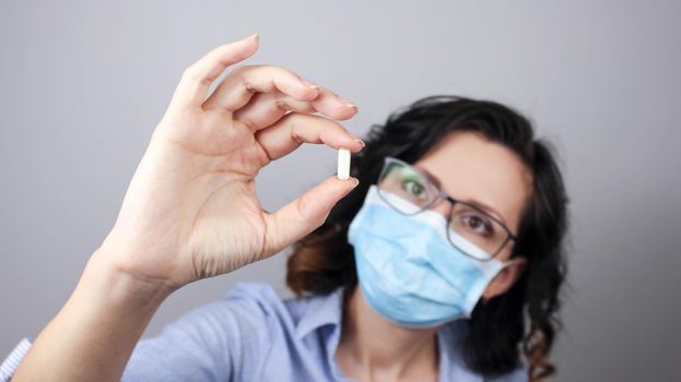 Woman wearing protection face mask against coronavirus and glasses. Woman in a mask showing medicine pill, vaccine. Medical mask, Close up shot, Select focus, Prevention from covid19