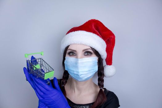 Woman wearing protection face mask against coronavirus. Woman in a mask and Christmas hat and holding shopping cart.