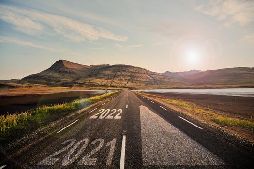 The word 2022 written on highway road in the middle of empty asphalt road at golden sunset and beautiful blue sky. Iceland. High-quality photo