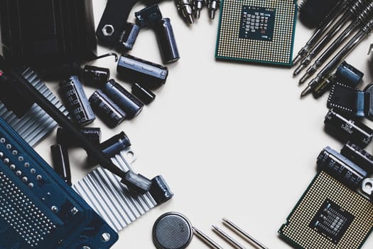 Top view of computer parts with CPU, fan cooler, battery, capacitors, radiator, chip, screwdrivers on white table background with copy space in the center. DIY constructor concept