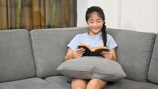 Pretty asian girl relaxing on comfortable sofa and reading book.