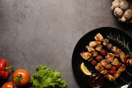 Grilled chicken meat skewers with fresh vegetables on dark stone background. Copy space for your text.