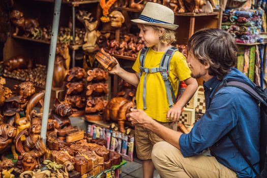 Dad and son at a market in Ubud, Bali. Typical souvenir shop selling souvenirs and handicrafts of Bali at the famous Ubud Market, Indonesia. Balinese market. Souvenirs of wood and crafts of local.