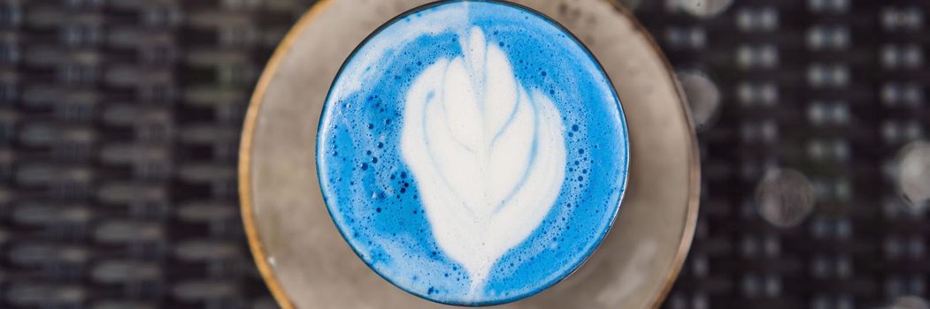 Trendy drink: Blue latte. Top view of hot butterfly pea latte or blue spirulina latte on gray textured background. Copy space for text. BANNER, LONG FORMAT