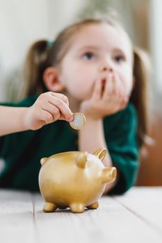 Little girl thinking about her money spending and putting a coin into a piggy bank. Economy, money saving and deposit concept. Selective soft focus