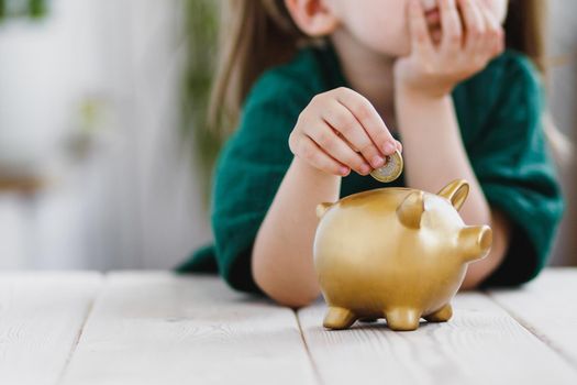 Little girl in green dress thinking about her money spending and putting a coin into a piggy bank. Economy, money saving and deposit concept. Selective soft focus