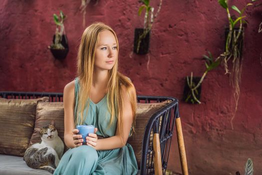 Young woman having a mediterranean breakfast seated at sofa and with her cat and drinks Trendy drink: Blue latte. Hot butterfly pea latte or blue spirulina latte.