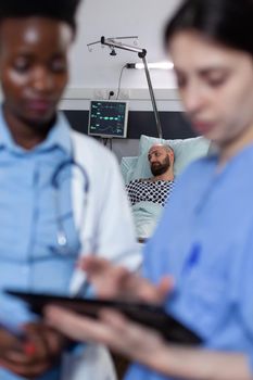 Doctor and nurse reading digital test results on tablet for man with low spo2 saturation waiting diagnosis. Patient with illness waiting while medical caregivers looking at imaging device.