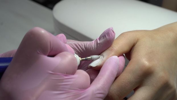 Young woman in the salon does a manicure. A manicurist uses a drill machine to remove nails. Closeup. 4k