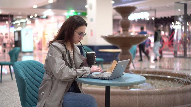 Young woman in a cafe with a laptop on the background of a fountain. Decoration in the cafe. 4k