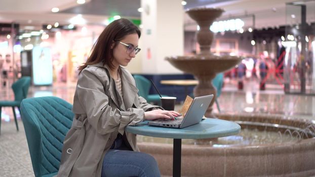 Young woman in a cafe with a laptop on the background of a fountain. Decoration in the cafe. 4k