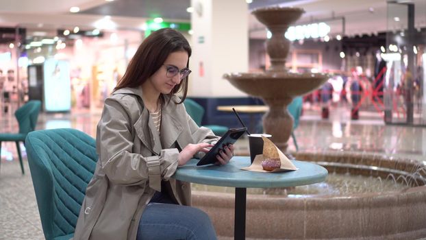 A young woman in a cafe with a tablet in her hands against the background of a fountain. Decoration in the cafe. 4k