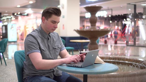 Young man in a cafe with a laptop on the background of a fountain. Decoration in the cafe. 4k