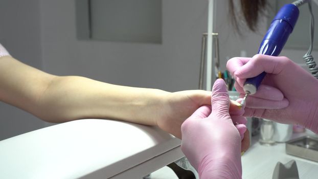 Young Asian woman with glasses in a manicure salon. A manicurist uses a drill machine to remove nails. The camera zooms in. 4k