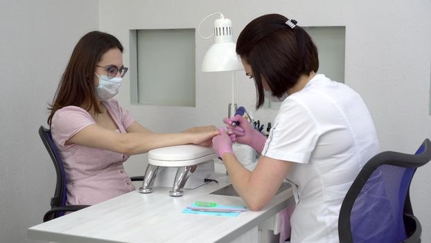 Young woman with glasses in a manicure salon. A manicurist uses a drill machine to remove nails. 4k