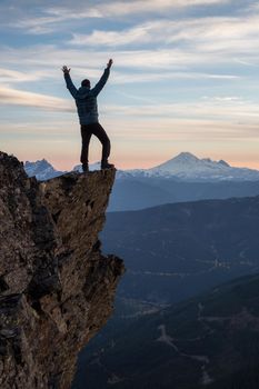 Adventurous man is standing on top of the mountain and enjoying the beautiful view during a vibrant sunset. Taken on top of Cheam Peak in Chilliwack, East of Vancouver, BC, Canada.