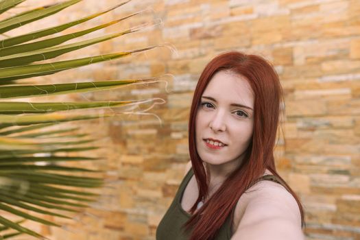 young woman taking a selfie with her cell phone on her summer vacation. tourist in hotel. self portrait in the foreground. natural light, outside, red-haired woman.