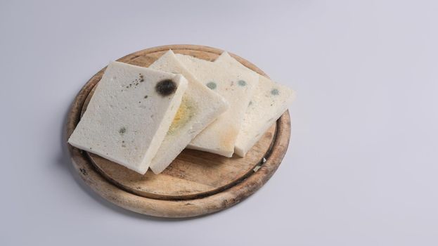 Moldy bread on wooden chopping board with white background.