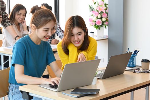 Two cheerful creative women discussing new project plan together in modern office.