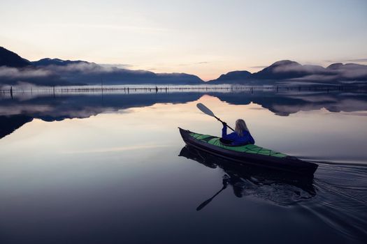 Adventurous Girl kayaking on an infatable kayak in a beautiful lake during a calm and peaceful sunrise. Taken in Stave Lake, East of Vancouver, British Columbia, Canada.