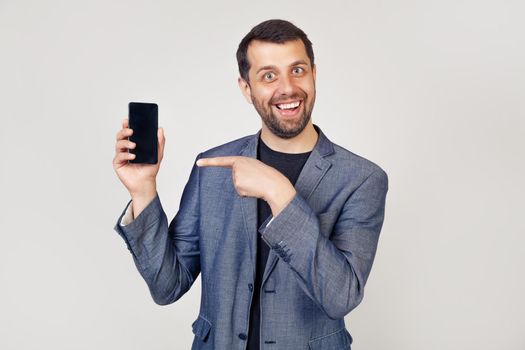 Cheerful businessman man looking at camera, showing smartphone screen, promote application hold smartphone pointing phone screen discuss profile on social networks smiling delighted recommend a phone