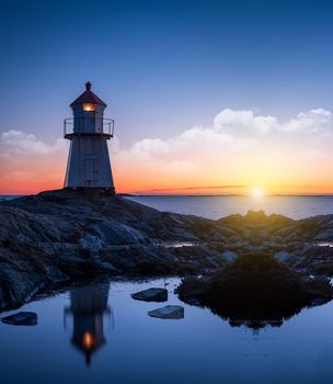 Lighthouse surrounded by rocks at night, lighthouse with lights on at sunset