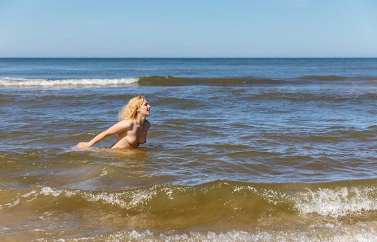 Lifestyle and nudity concept. Beautiful completely naked blonde woman enjoys nature on the seashore on a clear sunny day.