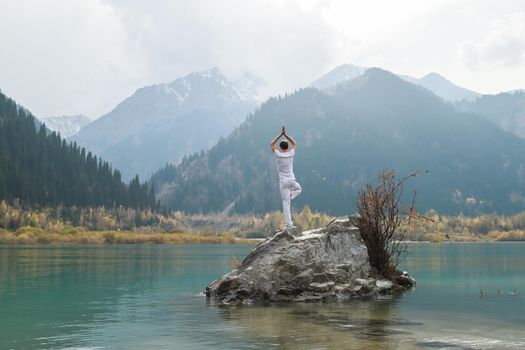 A zen man in white practices yoga in nature. Pose Vrikshasana or tree pose