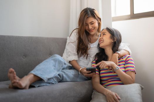 Two happy young asian casual women having fun using smartphone at home. Lesbian millennial couple concept