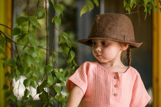 Portrait of happy cute little girl in rural style brown hat and muslin clothes on green background in a summer day.